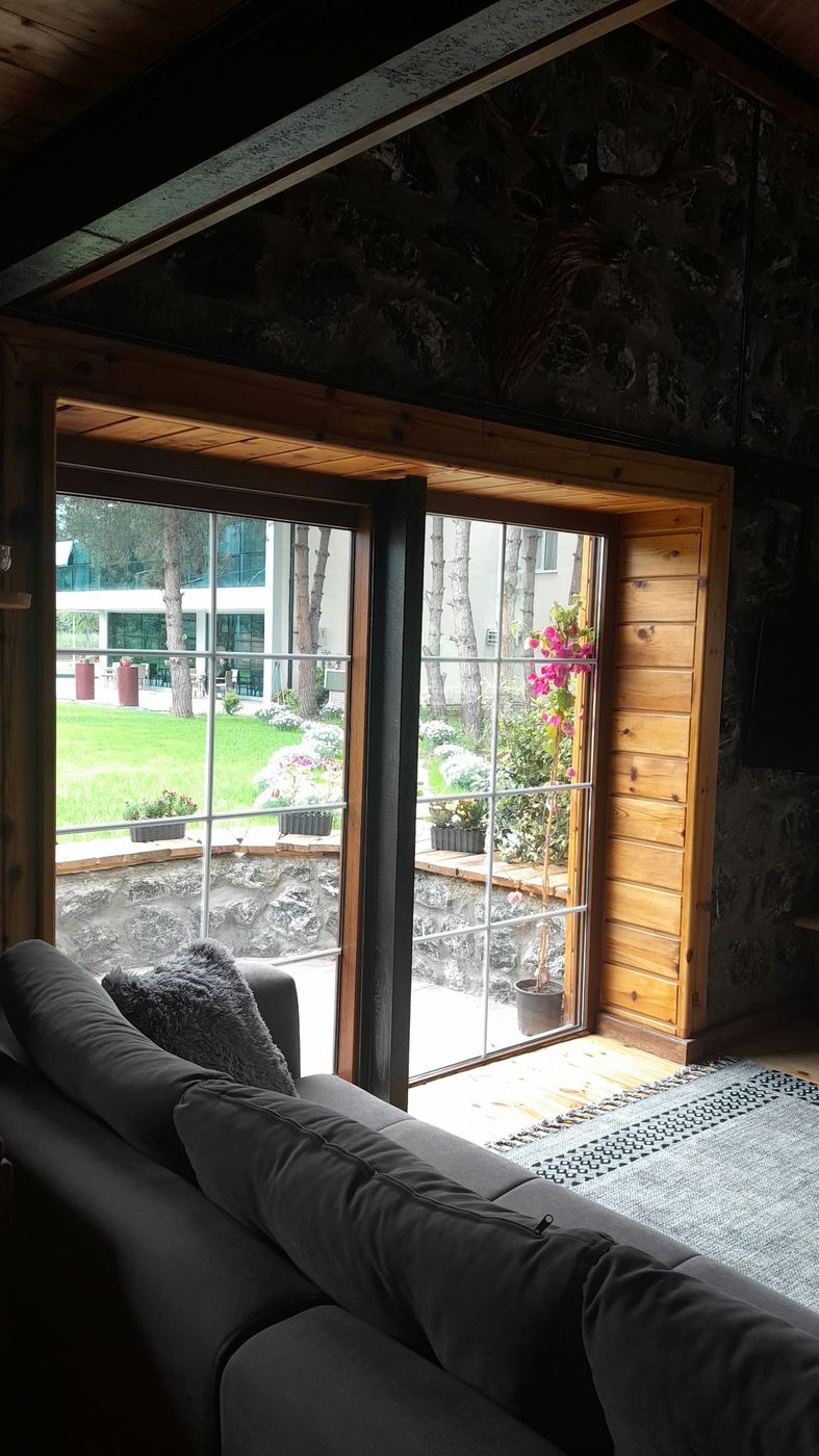 Taş evin penceresinden çamlar arasındaki bahçe ve otel binası